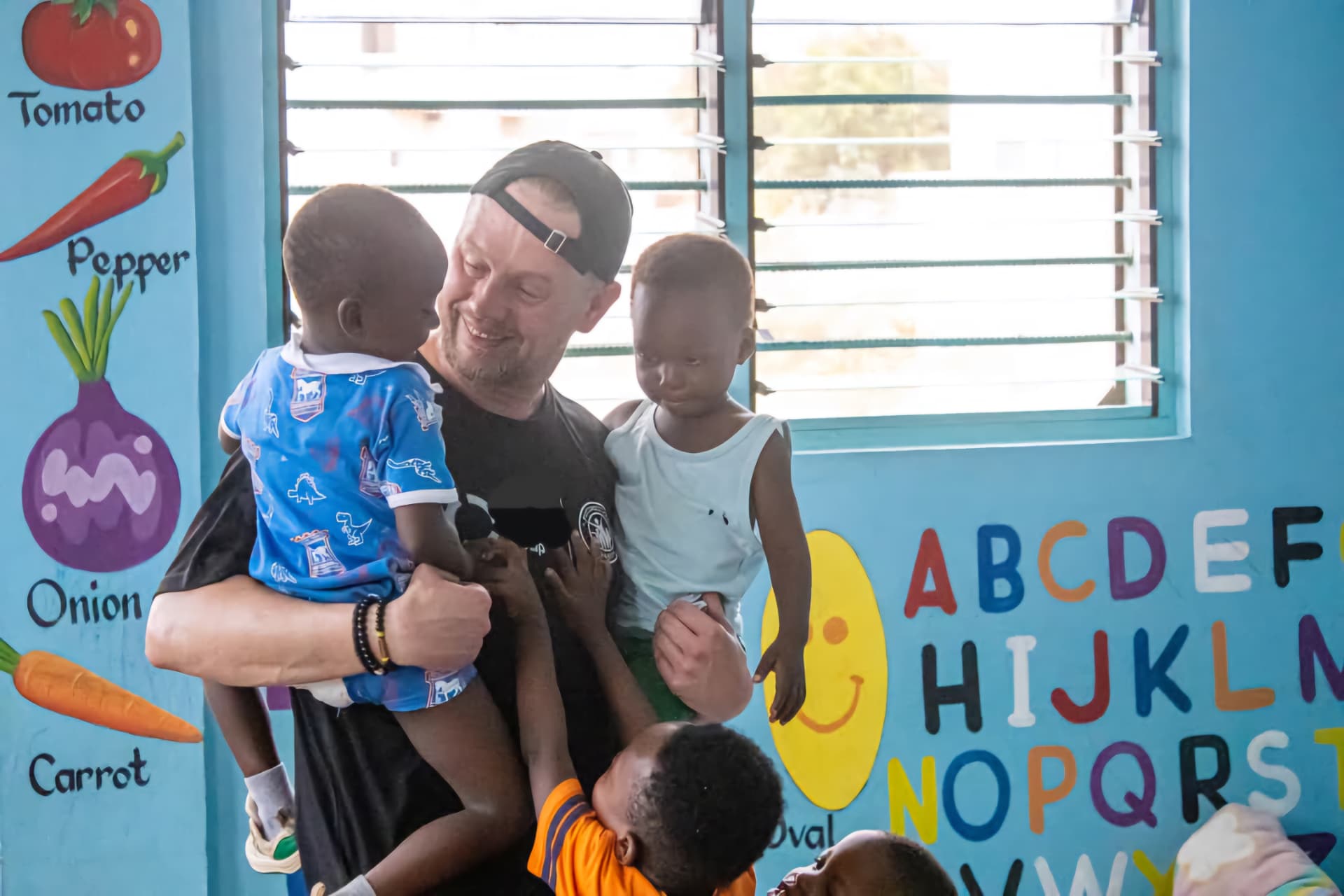 A volunteer holding two young children in a brightly painted classroom